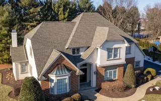 Two-story suburban house with a gabled roof, brick and stucco exterior, manicured lawn, and shrubbery, viewed from above on a clear day. Two-story suburban house with a gabled roof, brick and stucco exterior, manicured lawn, and shrubbery, viewed from above on a clear day.