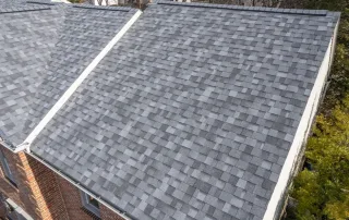Aerial view of two attached building rooftops with gray asphalt shingles and brick exterior walls. Aerial view of two attached building rooftops with gray asphalt shingles and brick exterior walls.