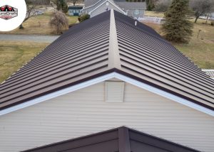Aerial view of a house roof with brown metal panels and beige siding, surrounded by a yard and trees. DuraCraft logo is visible in the upper left corner.